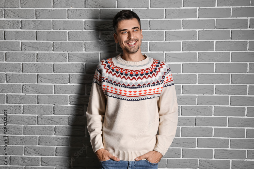 Handsome young man in knitted sweater near grey brick wall