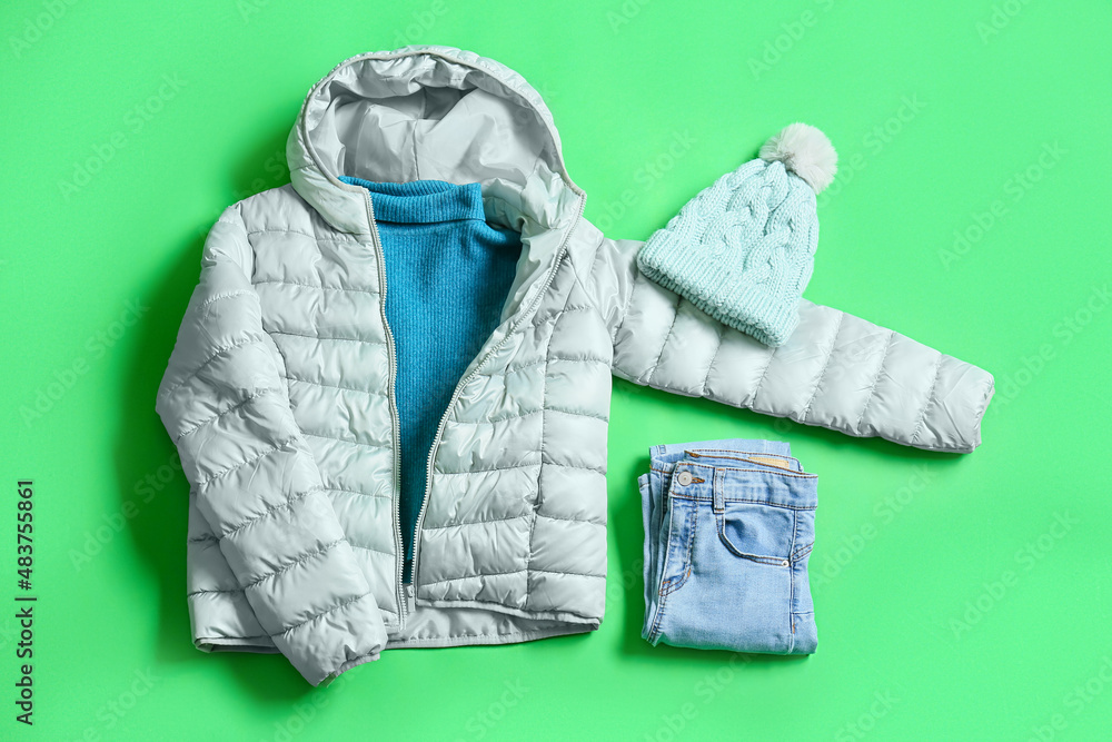 Winter jacket, sweater, knitted hat and jeans on green background