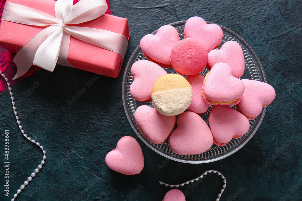 Dessert stand with tasty heart-shaped macaroons and gift box on black background