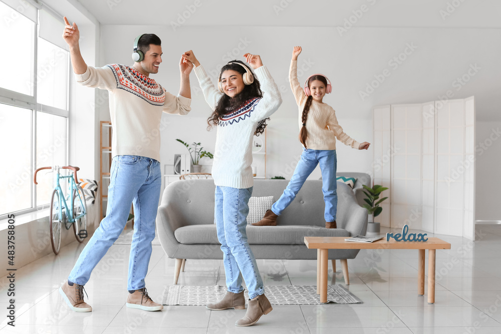 Happy parents with little daughter in warm sweaters and headphones dancing at home