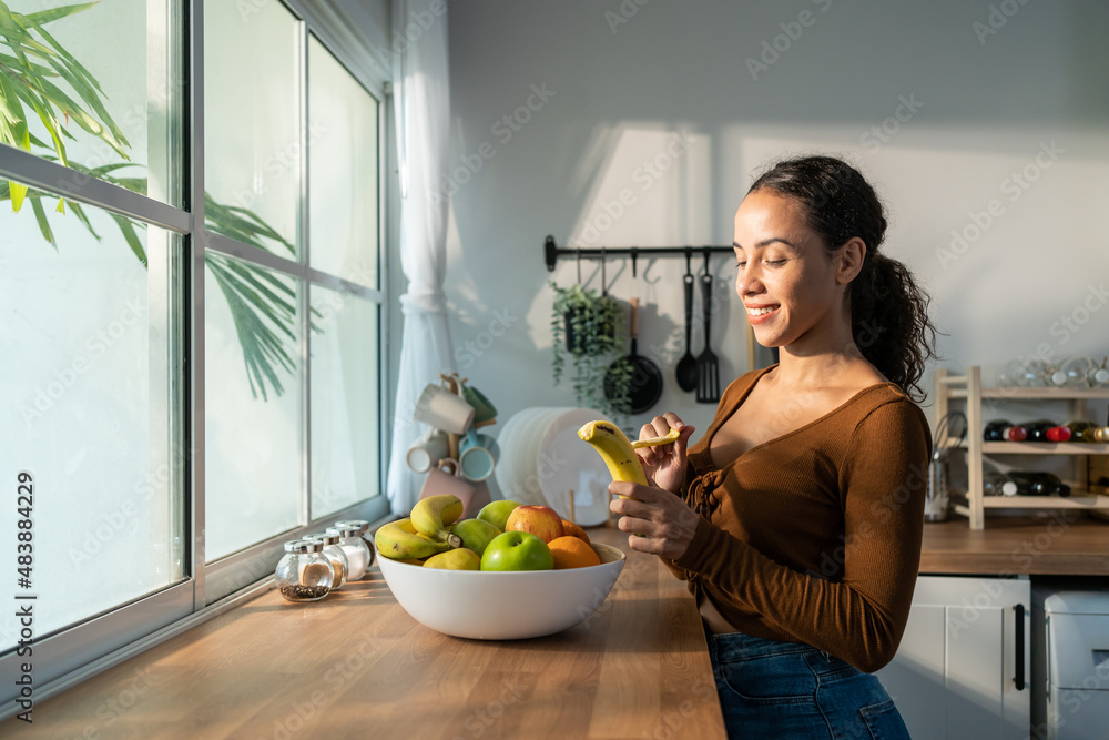 年轻漂亮的拉丁裔女性在家里厨房的桌子上吃水果。