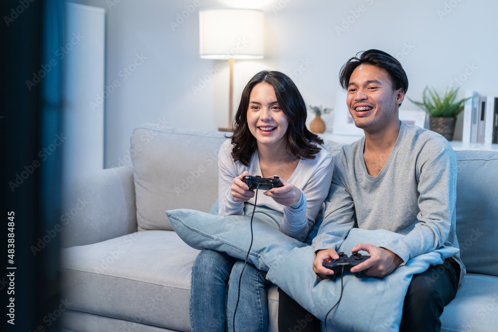 Asian young man and woman couple enjoy playing game together in house. 