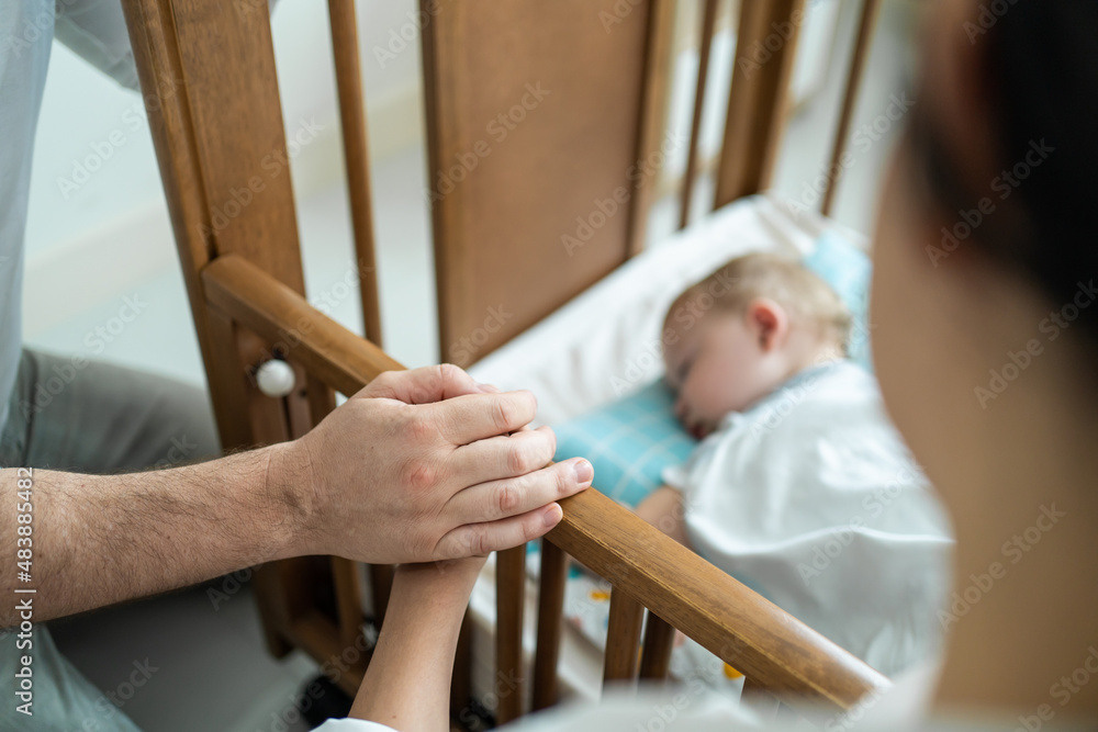 Close up of parents hand holding each other while look baby boy sleep. 