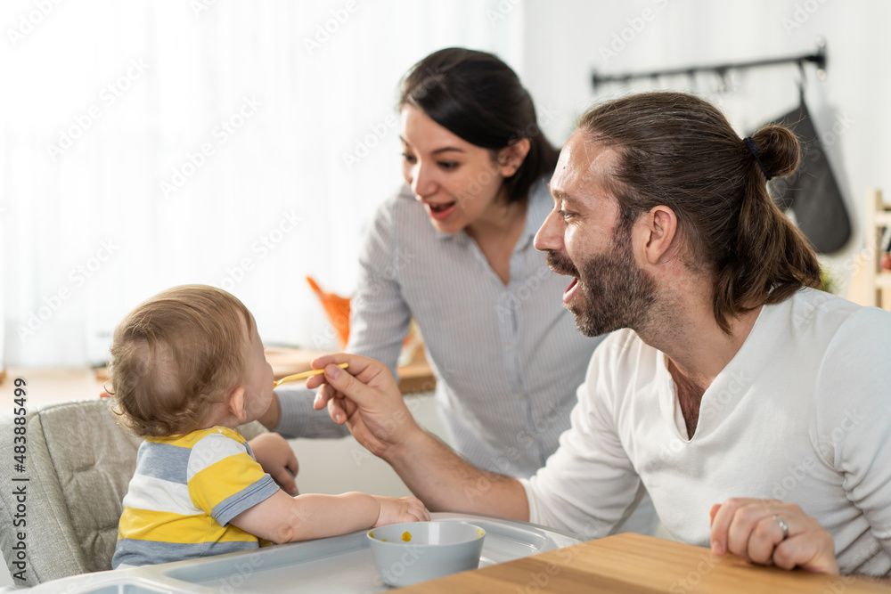 Caucasian beautiful parents take care of baby boy toddler in kitchen. 