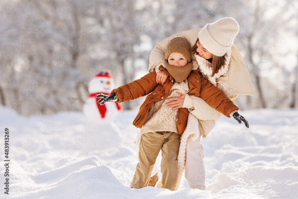 . happy family mother and child son playing, hugging and having fun near the snowman  on a winter wa