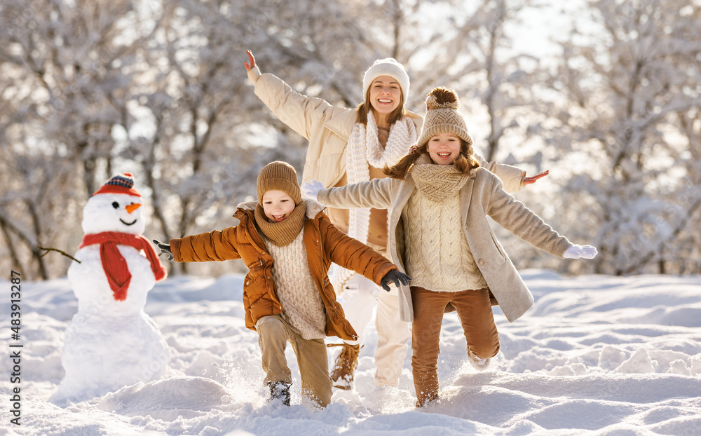 happy family mother and children playing, running and having fun near the snowman  on a winter walk 