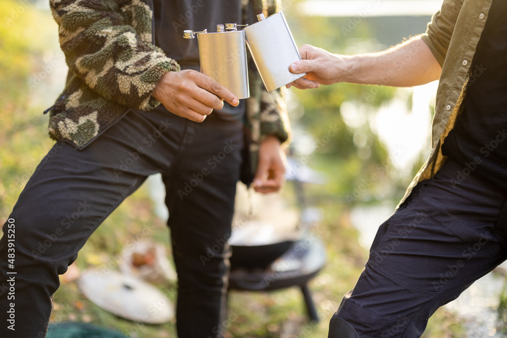 Two men cheering with flasks while fishing on lake, close-up on flask with empty space to copy paste