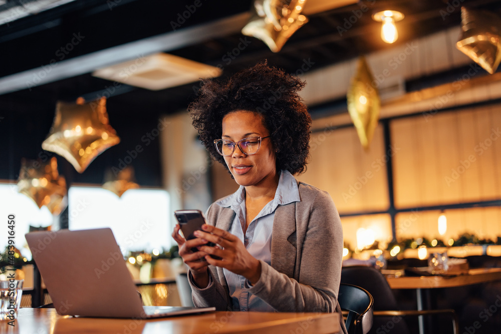 Relaxed African-American woman, checking her phone for messages, in the eatery.