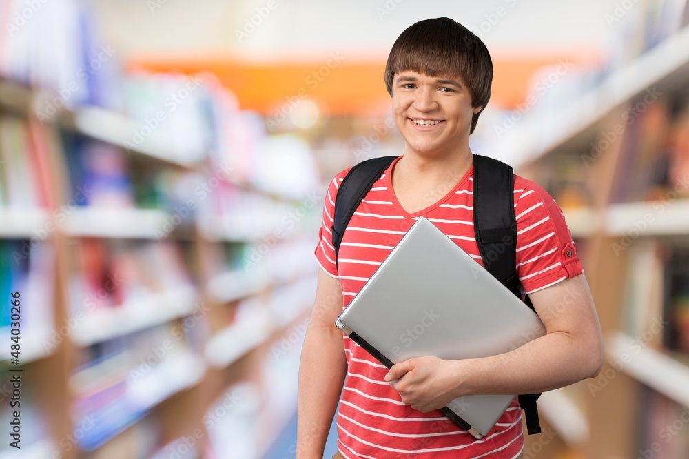 Portrait of cheerful student, learning accessories standing near bookshelves at library