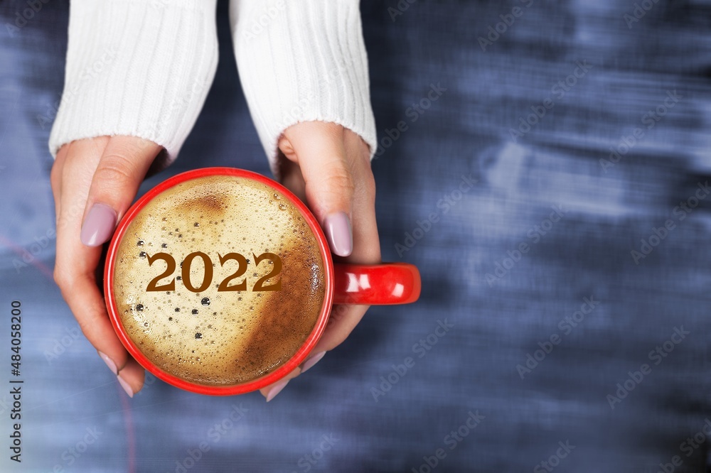 Number 2022 on the surface of cappuccino served in cup holding by female hands