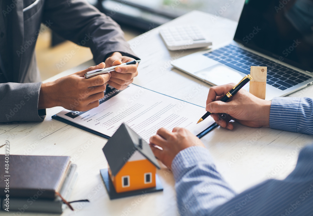 real estate agent assisting client to sign contract paper at desk with house model, house agency and