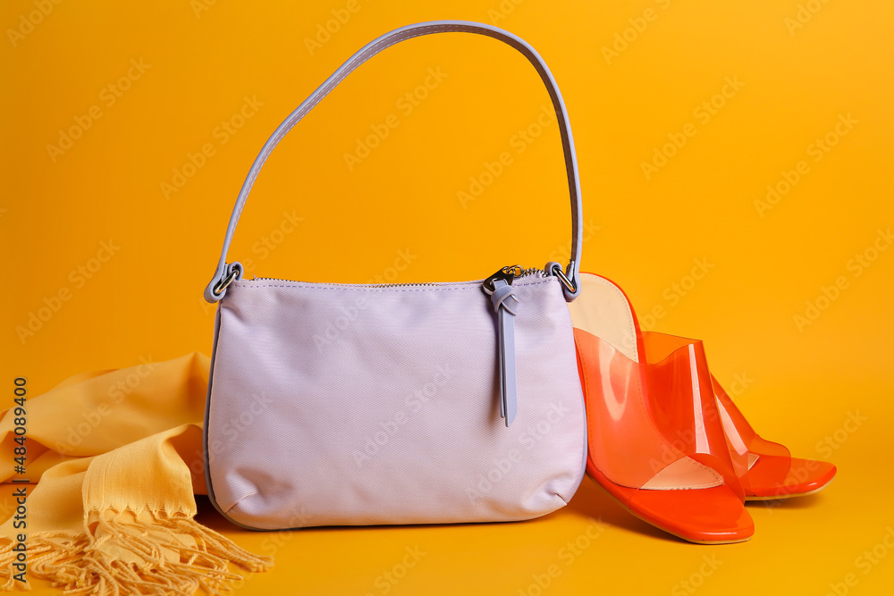 Stylish handbag, shoes and scarf on color background