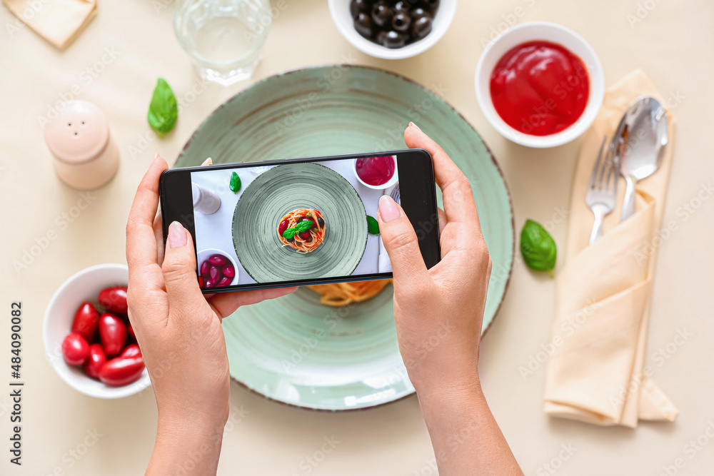 Woman taking picture of tasty Pasta Puttanesca in restaurant