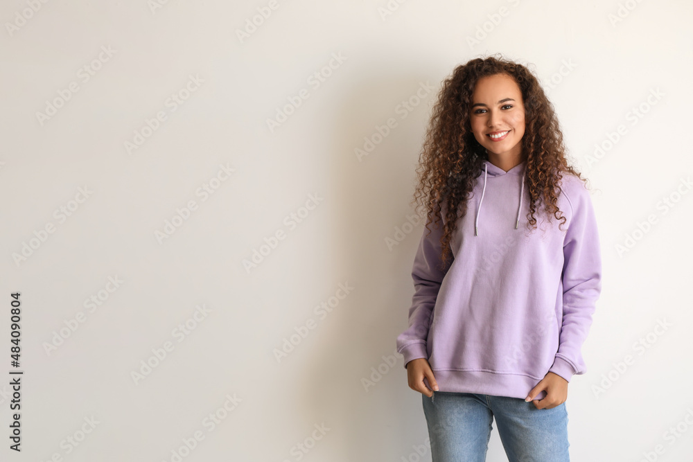 Beautiful young African-American woman in stylish hoodie on light background