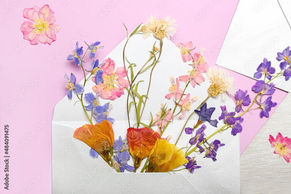 Envelope with dried pressed flowers on pink background, closeup