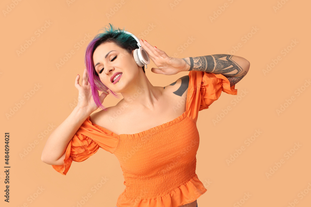 Beautiful woman with unusual hair and tattoo listening to music on orange background