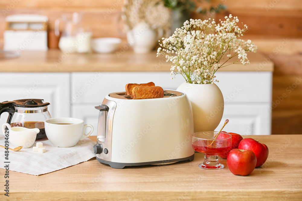 White toaster with bread slices, jam, apples and vase on table in kitchen