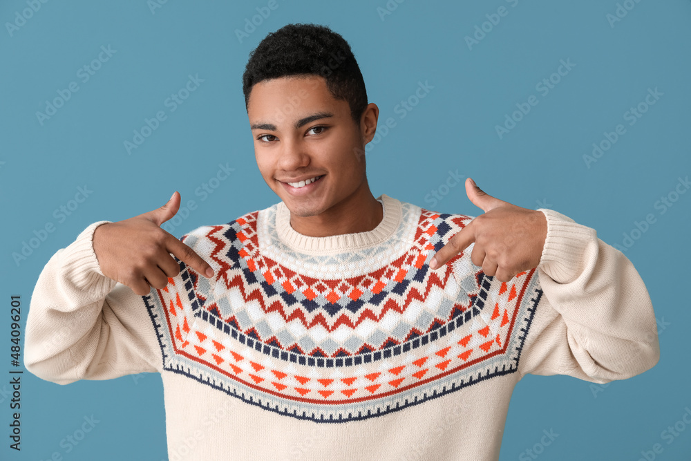 Handsome African-American guy in knitted sweater on color background