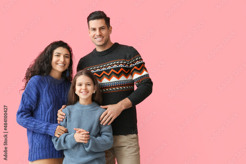 Little girl and her parents in warm sweaters on pink background