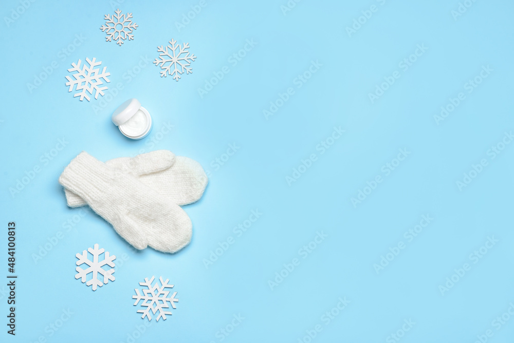 Jar with cream, knitted mittens and snowflakes on color background