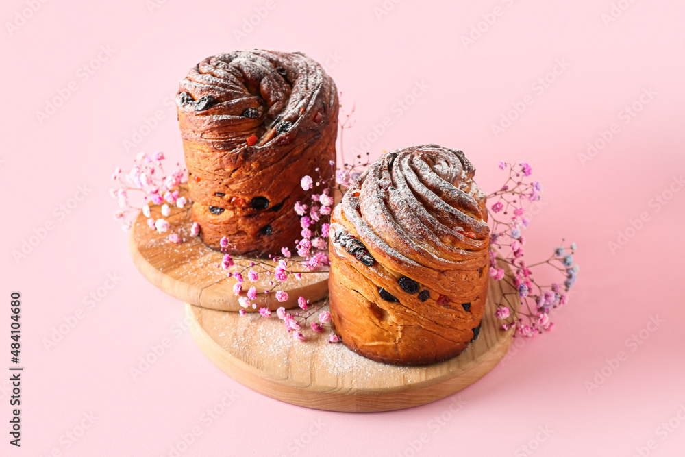 Wooden board with delicious Easter cakes and gypsophila flowers on pink background