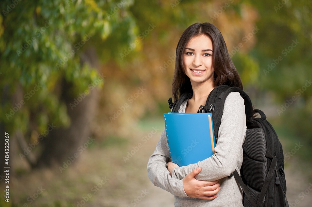 女学生站在户外，手里拿着书。