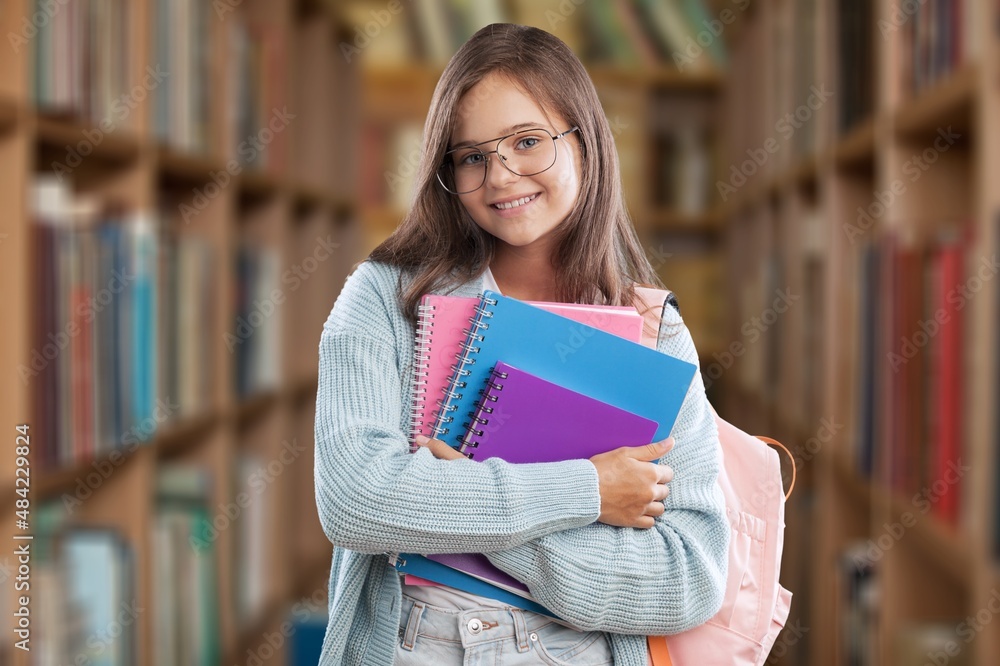 Portrait of cheerful student with backpack, learning accessories standing near bookshelves at librar