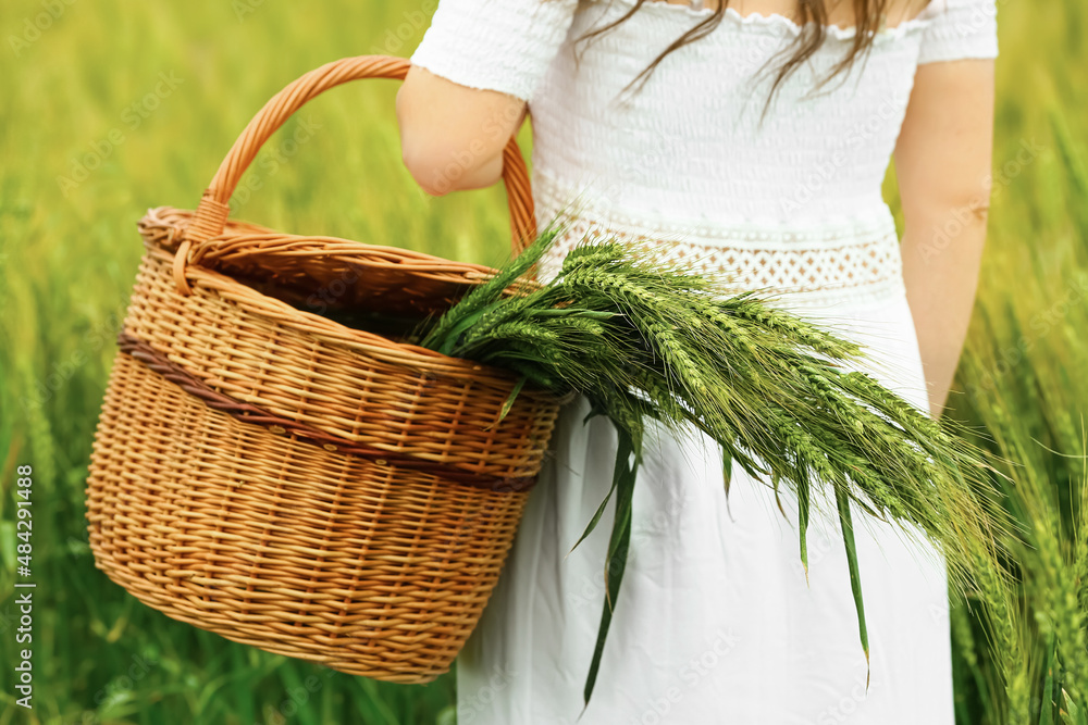 Woman holding wicker basket with green spikelets in field