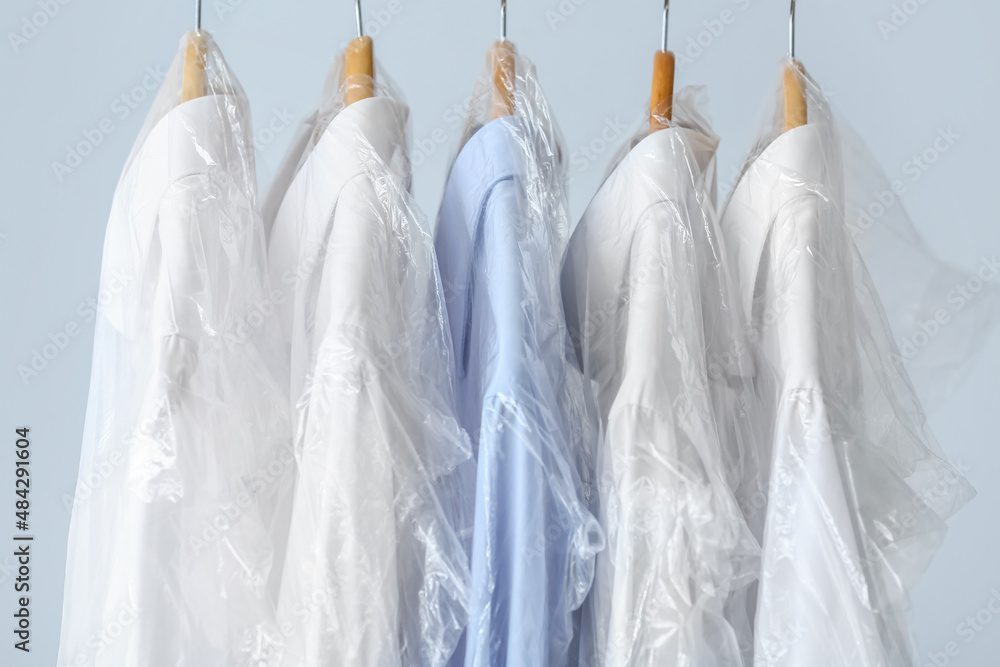 Rack with clean shirts in plastic bags on grey background