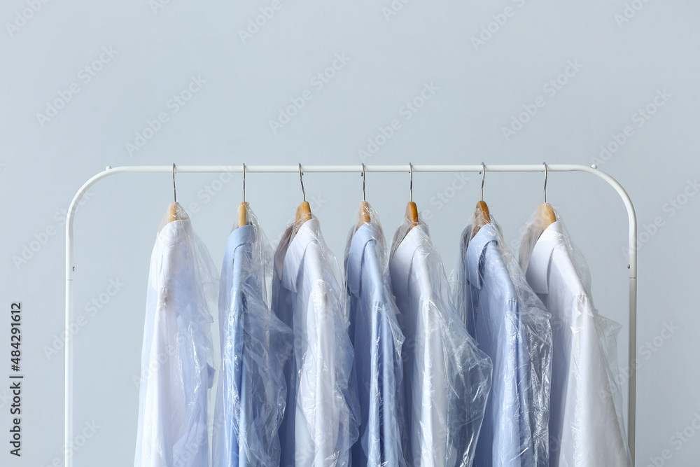 Rack with clean shirts in plastic bags on grey background