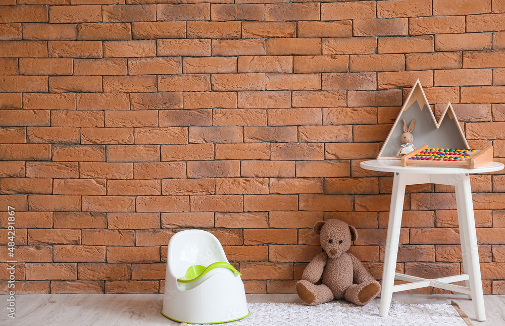 White potty and table with toys on floor near brick wall