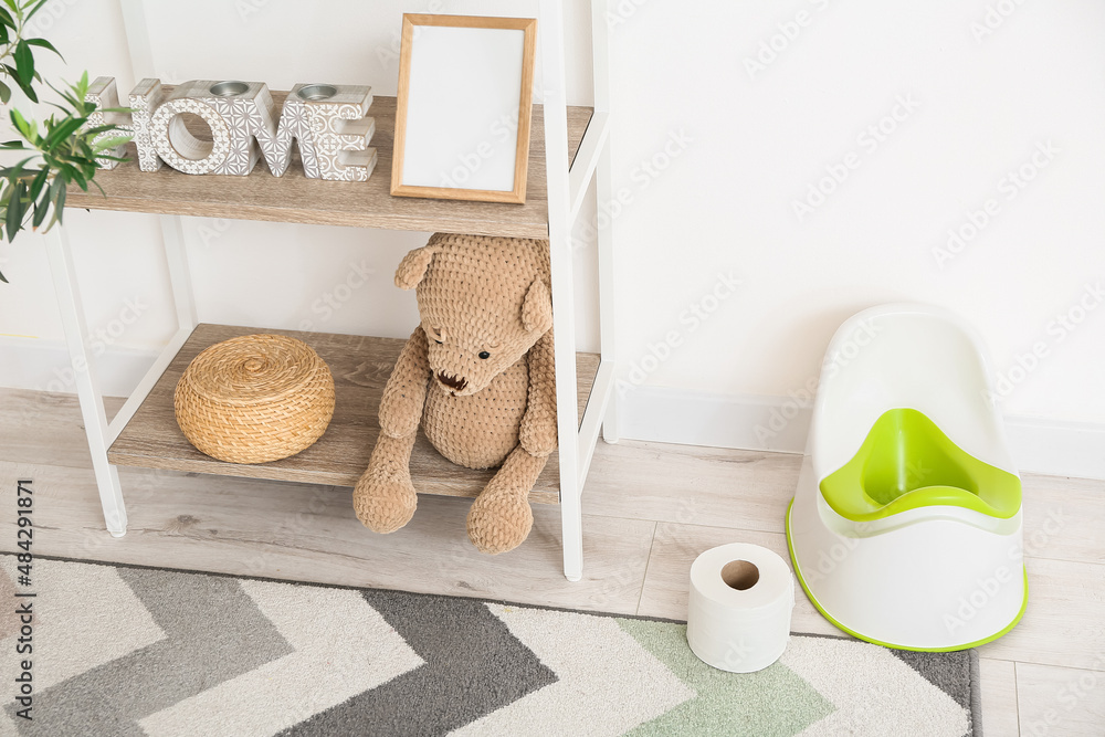 Shelf unit with toys, potty and toilet paper roll on floor near white wall