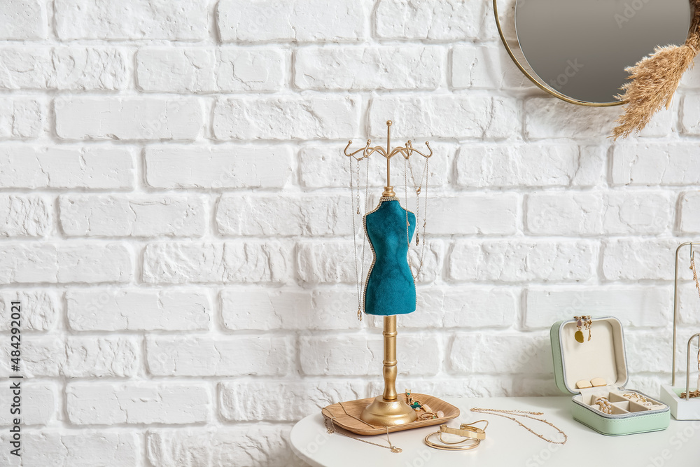 Stand and box with jewelry on table near white brick wall