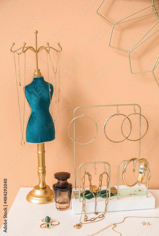 Stands with stylish jewelry and perfume bottle on white table near color wall