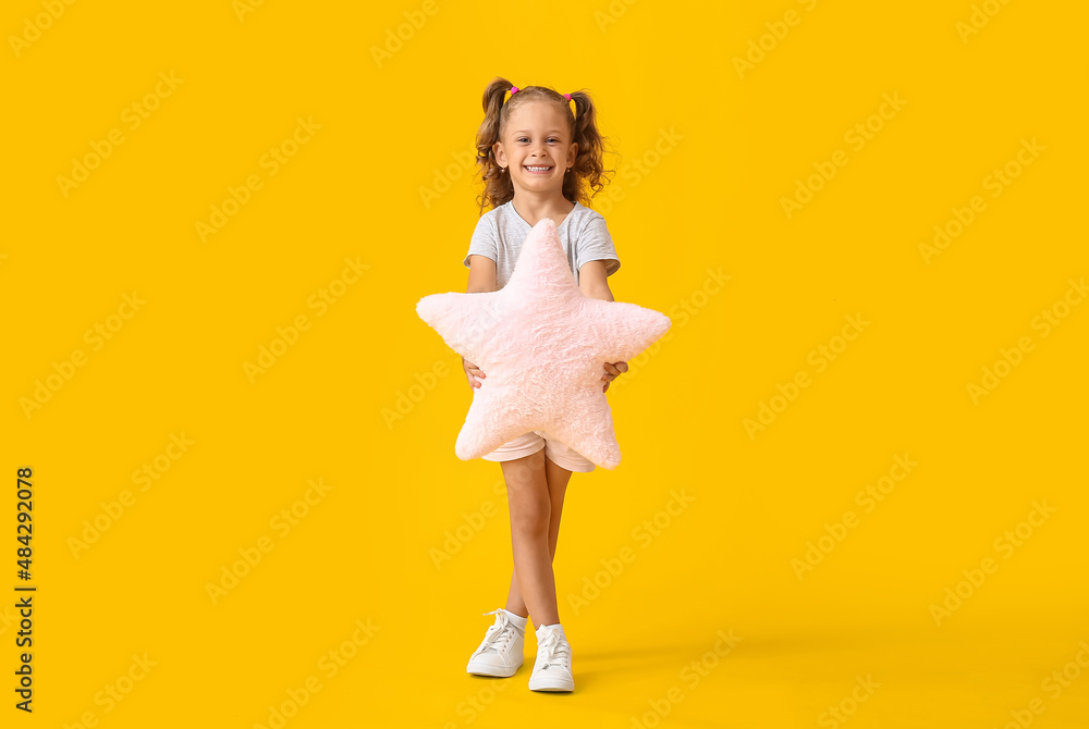 Adorable little girl with pillow in shape of star on yellow background