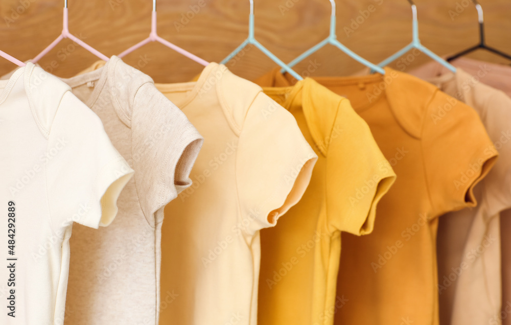 Baby bodysuits hanging near wooden wall, closeup