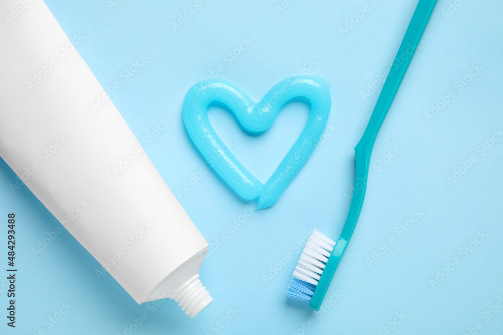 Heart made of toothpaste, tube and brush on blue background, closeup