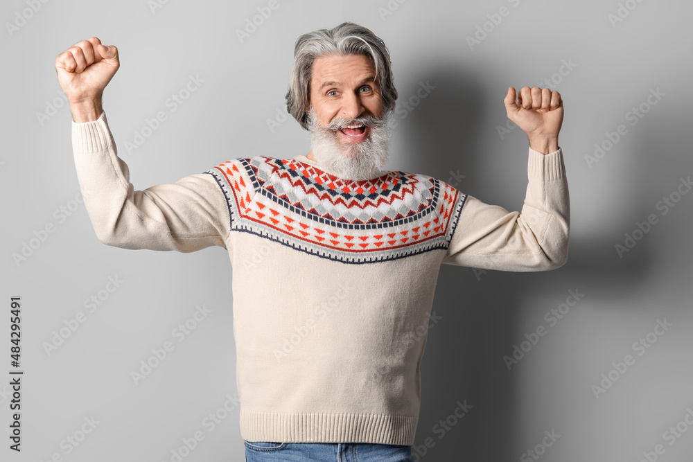 Handsome happy senior man in knitted sweater on grey background