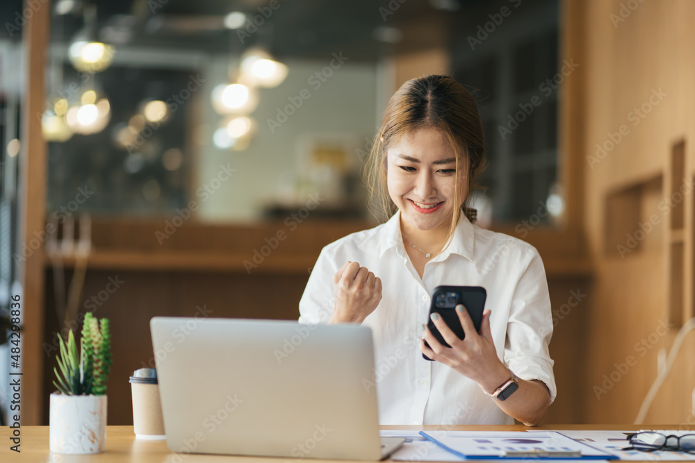 兴奋的年轻女性坐在桌旁，拿着笔记本电脑庆祝成功