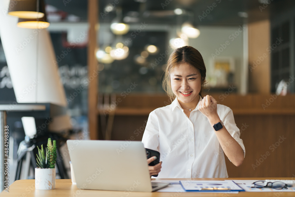 Excited young woman sitting at table with laptop and celebrating success