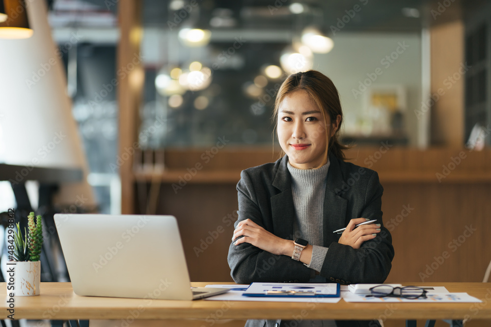 一位面带微笑的商务女性，坐在现代办公桌旁，拿着笔记本电脑工作