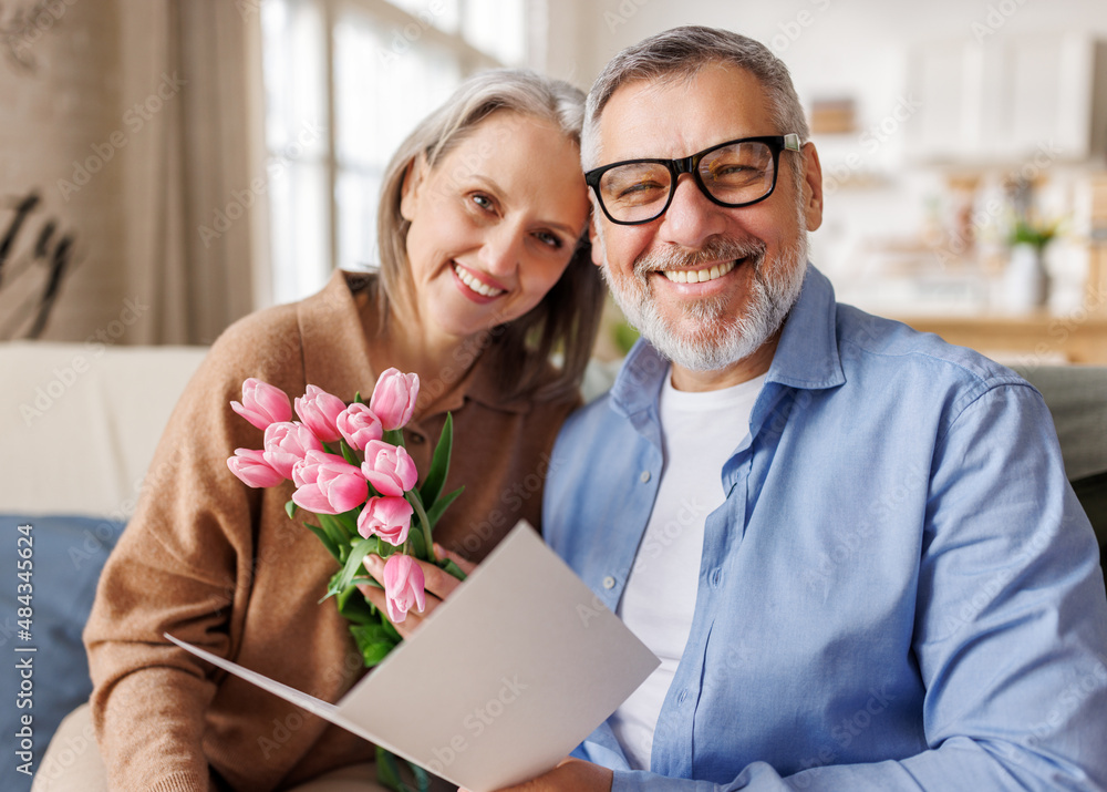 happy couple of elderly lovers congratulate each other on Valentines Day and give a postcard and fl