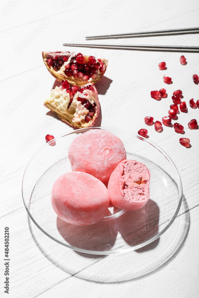 Plate with delicious mochi, pomegranate and chopsticks on white wooden background