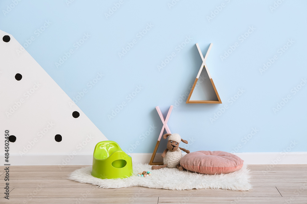 Green potty, toy sheep and pillow on grey wooden floor near color wall