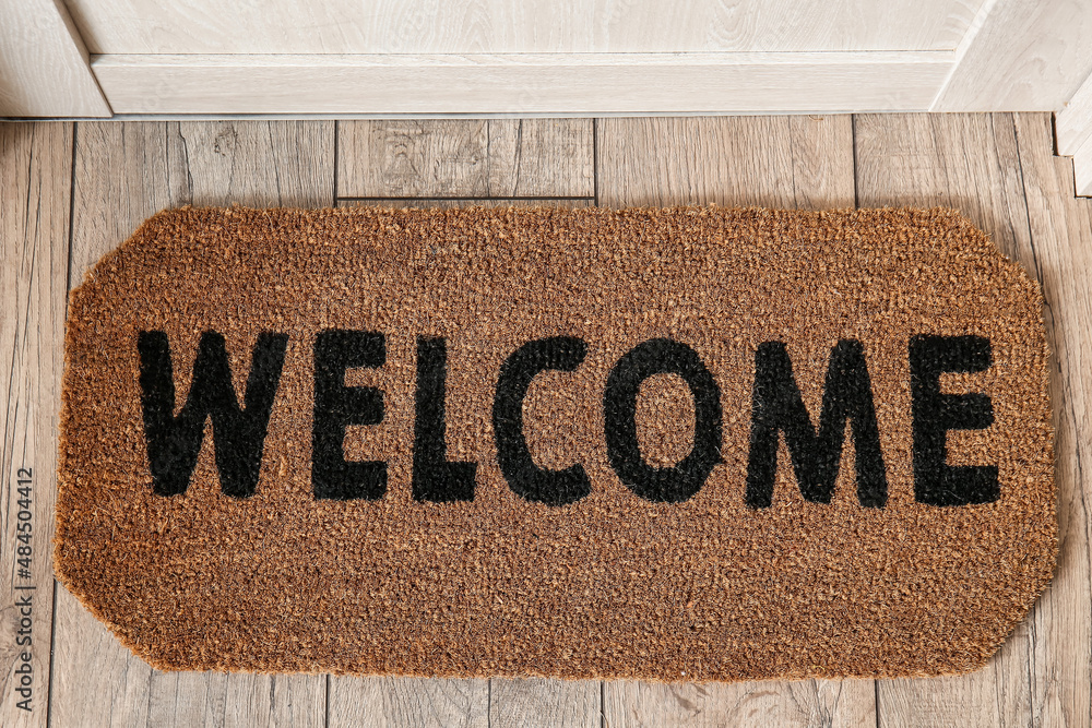 Stylish door mat with word WELCOME on floor in hallway