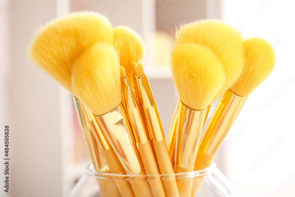 Glass with set of makeup brushes on table, closeup