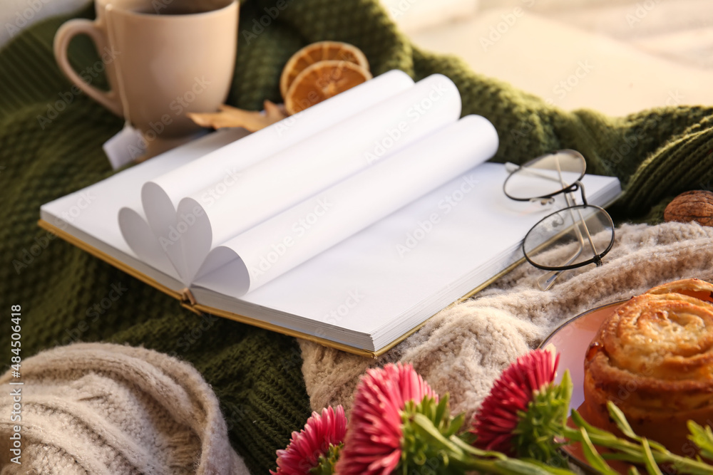 Blank book, cup of tea and flowers on plaid in room, closeup