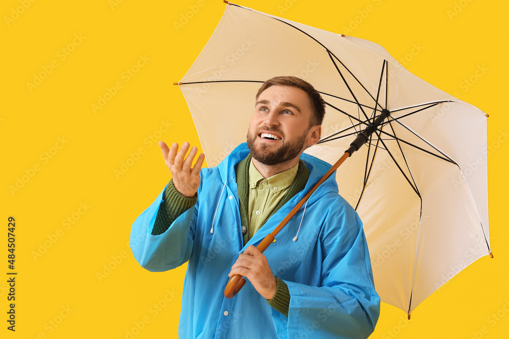 Young man in stylish raincoat and with umbrella on color background