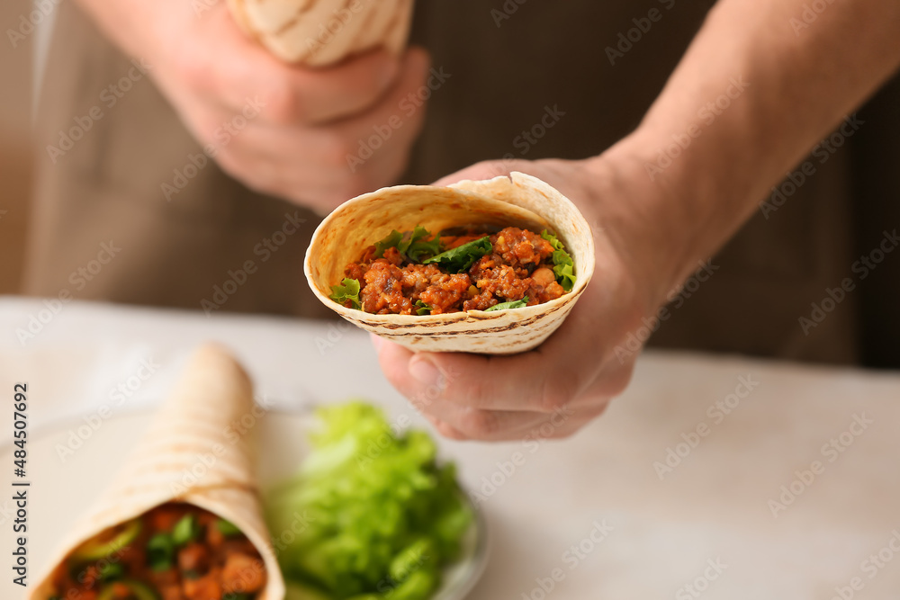 Man holding tasty burrito at table, closeup