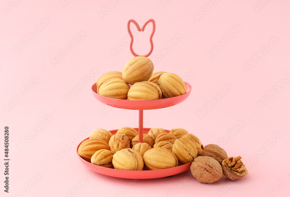 Dessert stand of tasty walnut shaped cookies with boiled condensed milk on pink background